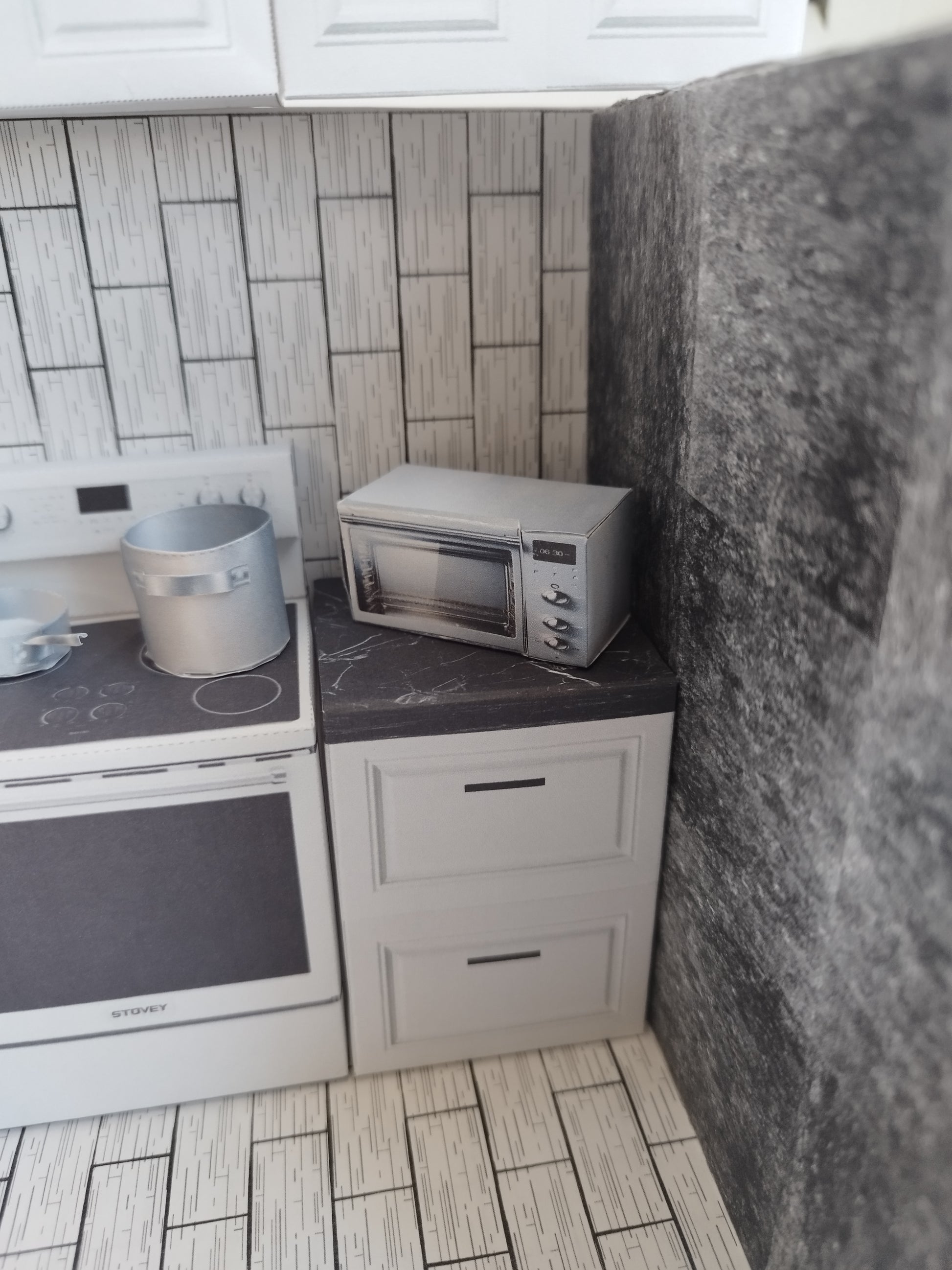 A digital printable template for a 1:12 scale dollhouse kitchen cabinet and drawer set, designed for BMM system dollhouse setups. The template features detailed, modern cabinets with drawers, ready to be printed on regular paper, cut, and assembled for a miniature kitchen scene.