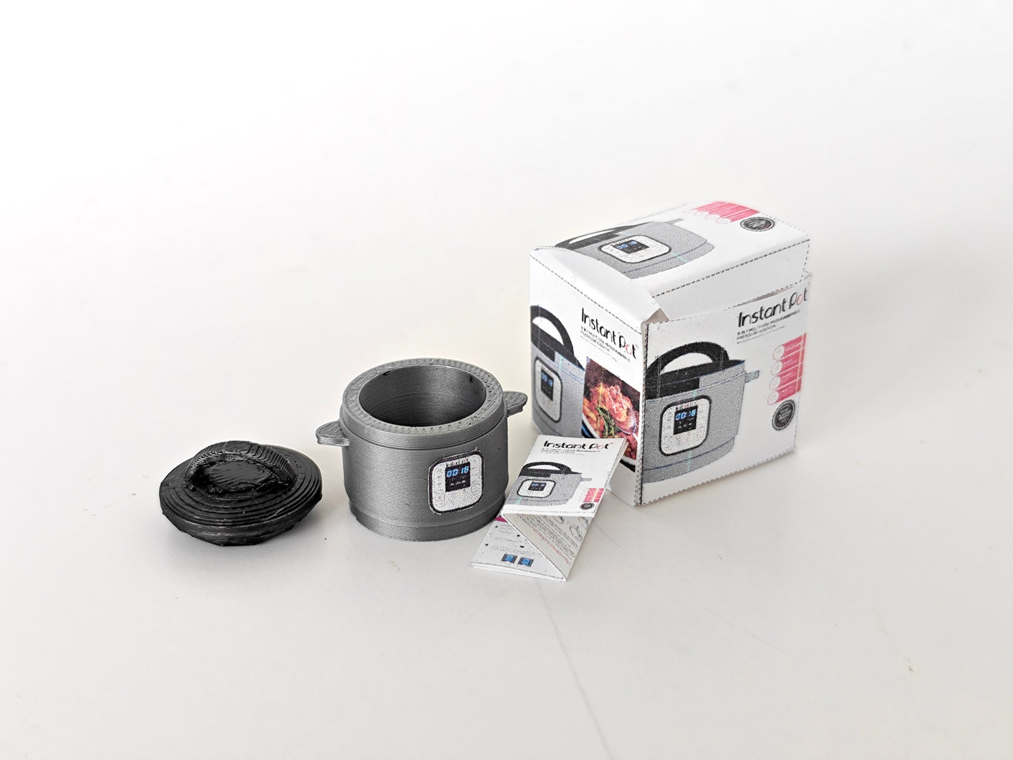 "A 3D-printable STL file of a 1:12 scale miniature Instant Pot, featuring detailed buttons and a lid for a realistic dollhouse kitchen appliance