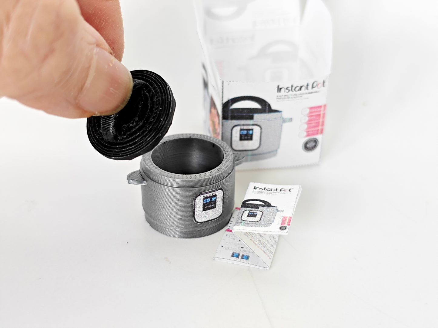 "A 3D-printable STL file of a 1:12 scale miniature Instant Pot, featuring detailed buttons and a lid for a realistic dollhouse kitchen appliance