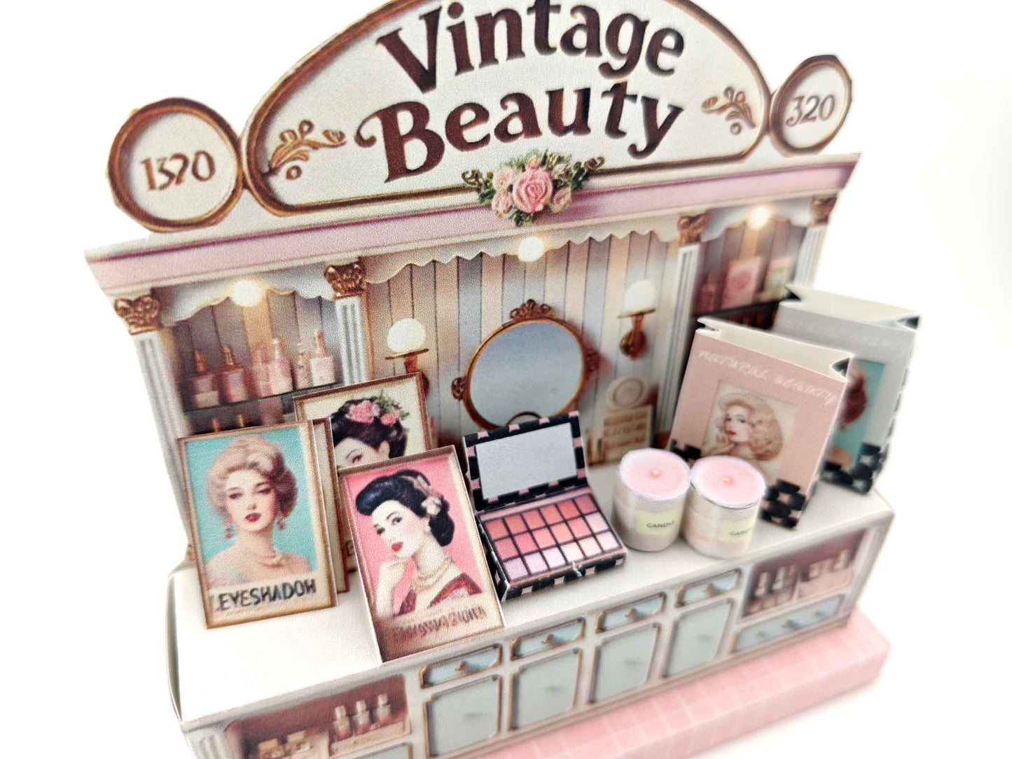 A digital image of a DIY vintage makeup counter miniature scenery kit made from cardstock. The kit features a foldable counter with a retro design, a small makeup box, a colorful poster with floral accents, and a detailed eyeshadow palette, arranged for a dollhouse display.