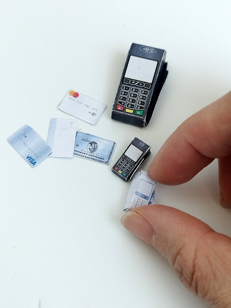 Overhead view of miniature paper credit card machines and various cards on a white surface.