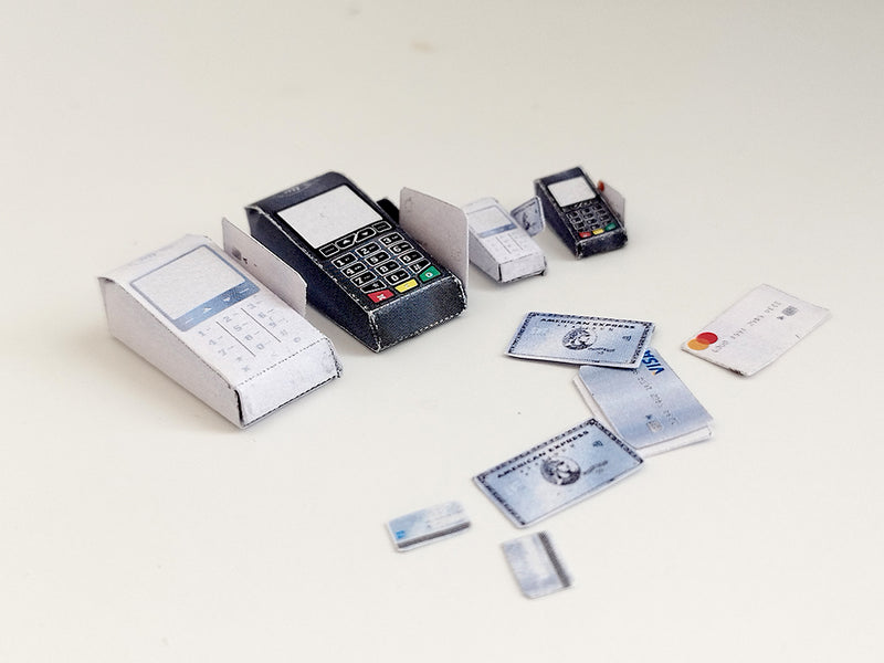 Overhead view of miniature paper credit card machines and various credit cards on white.