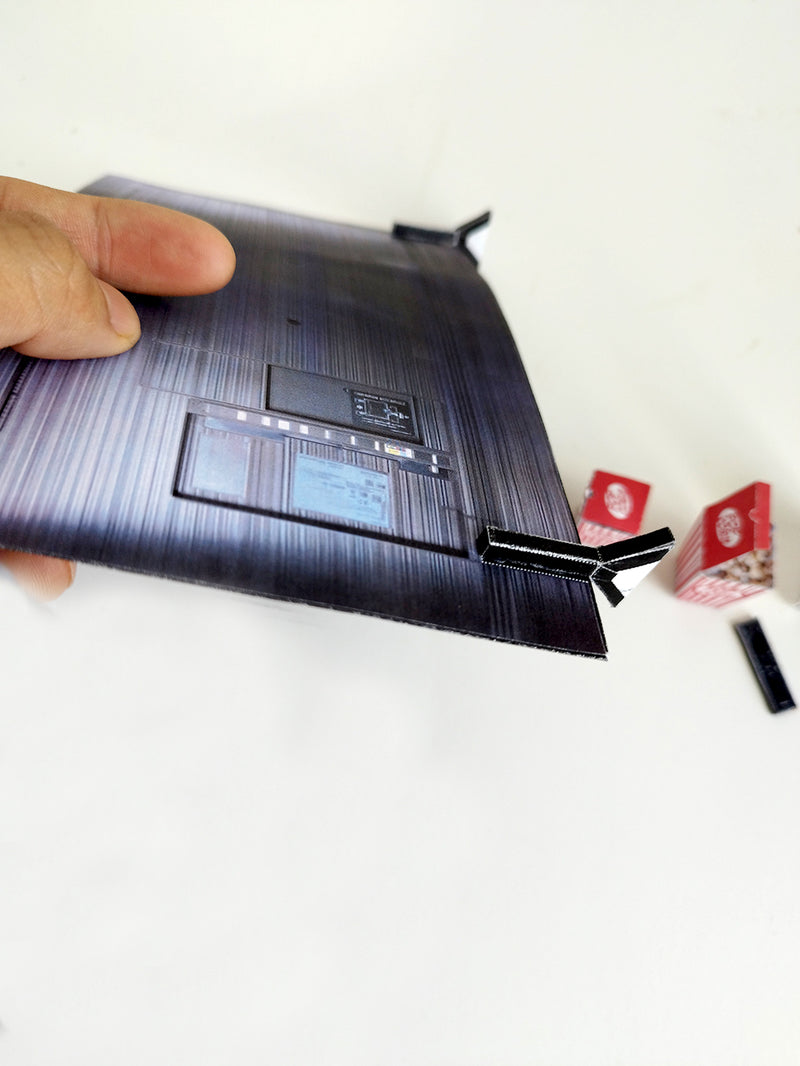 Hand holding a miniature dark grey brushed TV back with small red popcorn boxes.