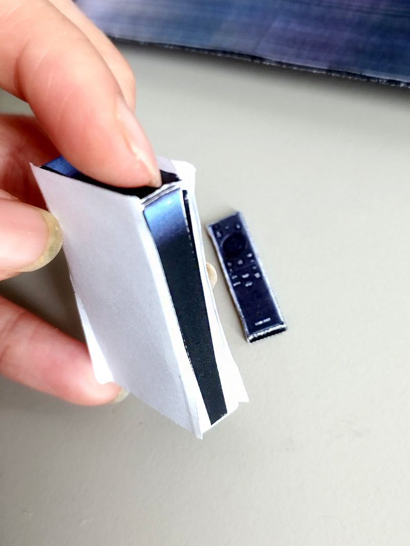 Hand holding a miniature white and black game console with a tiny black remote.