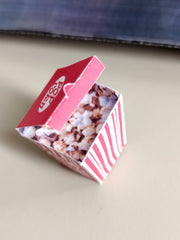 Miniature red and white striped popcorn box with 'POP CORN' on its open lid.