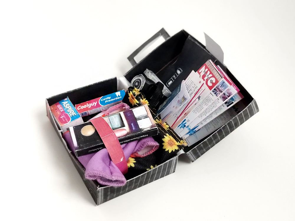 Miniature black and white striped luggage open, revealing doll toiletries and NYC map.