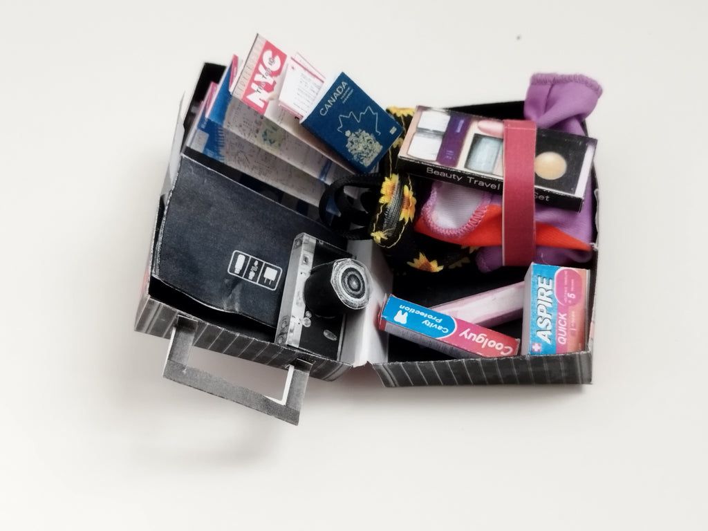 Miniature open luggage with a Canada passport, NYC map, camera, and beauty set.