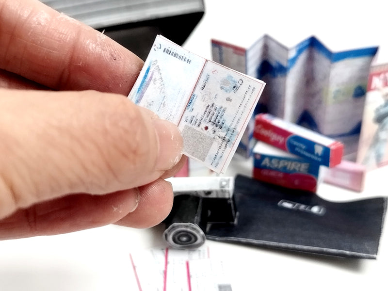 Hand holds a miniature document, with tiny blue map, red boxes, and black luggage.