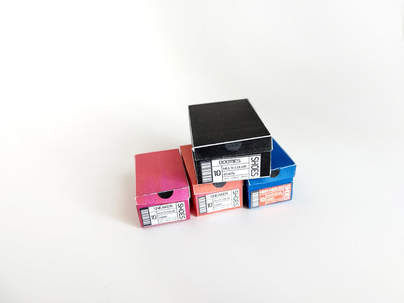Miniature black, red, and blue shoe boxes stacked on a white surface.