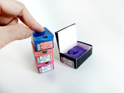 Hand stacking tiny colorful shoe boxes, one open with purple booties.