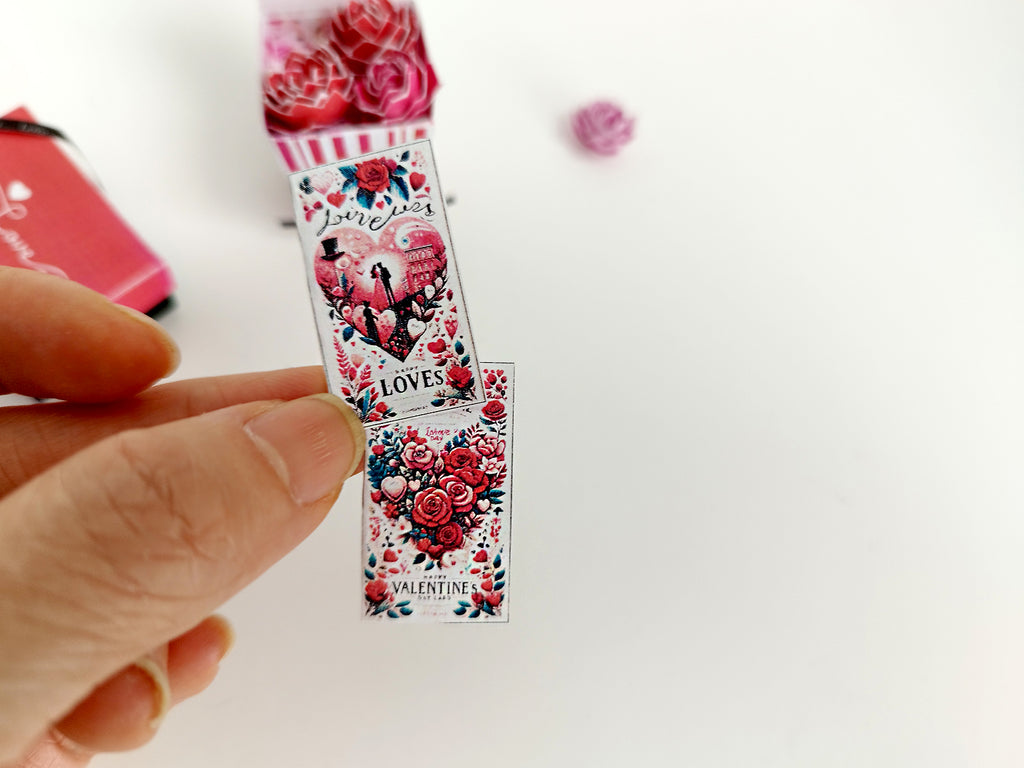 Hand holding two miniature Valentine's cards with red roses and hearts.