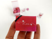 Hand holding a miniature red 'Love' gift box with a black ribbon.