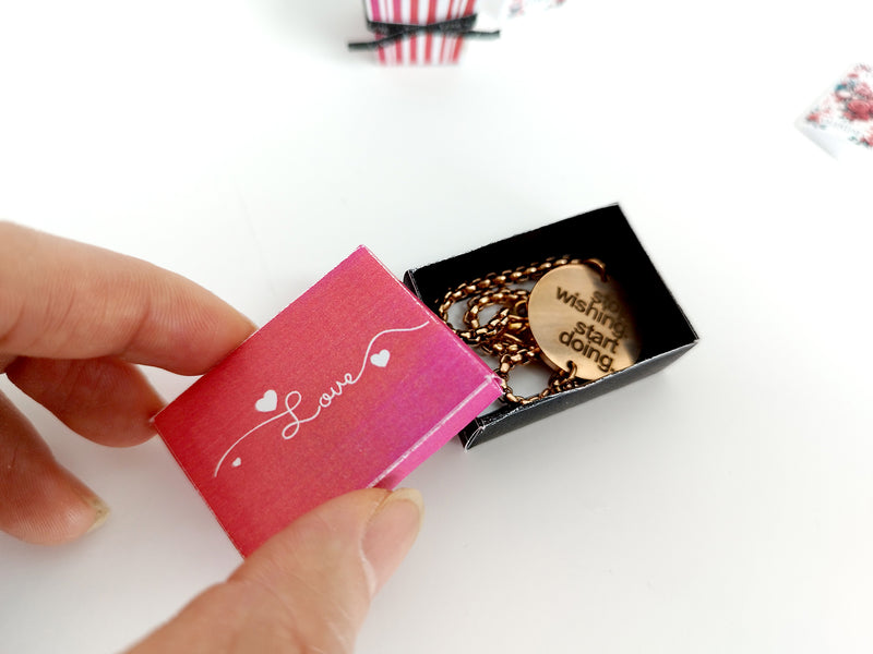 Miniature pink 'Love' gift box held open, revealing a gold pendant necklace.