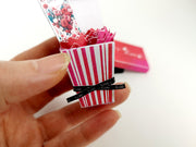 Hand holds miniature pink striped box with folded paper flowers and 'Love' ribbon.