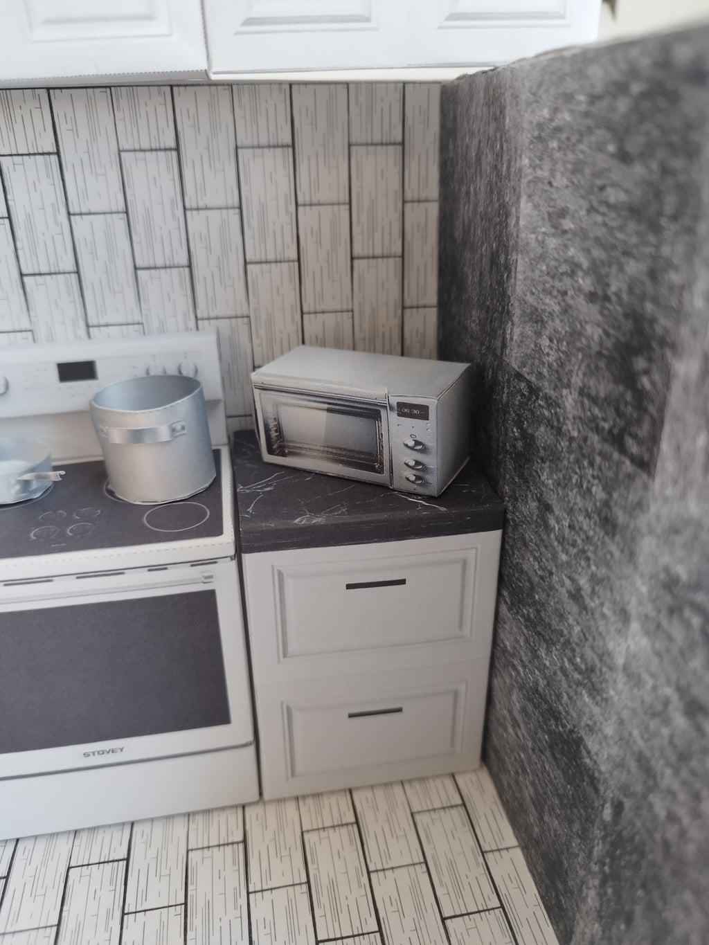 A digital printable template for a 1:12 scale dollhouse kitchen cabinet and drawer set, designed for BMM system dollhouse setups. The template features detailed, modern cabinets with drawers, ready to be printed on regular paper, cut, and assembled for a miniature kitchen scene.


