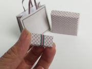 A 1:6 scale printable dollhouse set featuring four luxury brand-inspired brown shopping bags, a purse, and boxes, designed for department store or luxury home decor dioramas, ideal as yearly ornaments for miniature scenes.