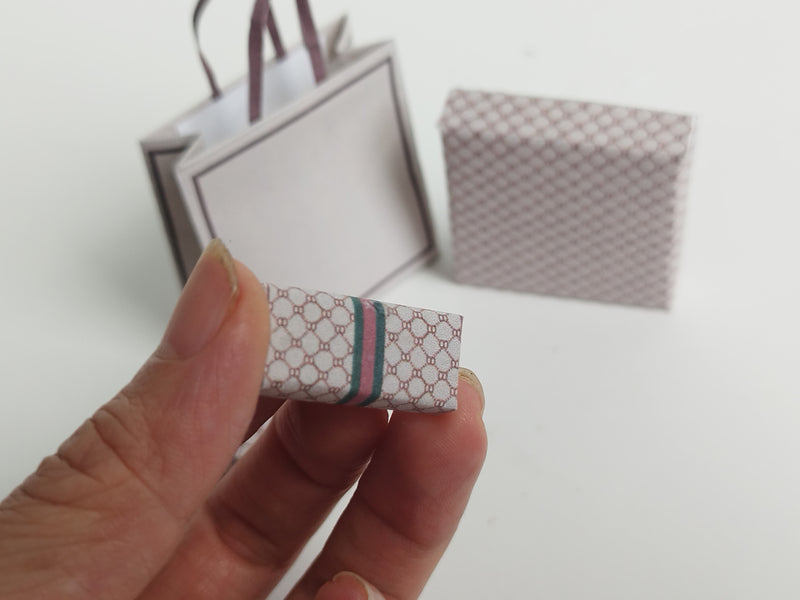 A 1:6 scale printable dollhouse set featuring four luxury brand-inspired brown shopping bags, a purse, and boxes, designed for department store or luxury home decor dioramas, ideal as yearly ornaments for miniature scenes.