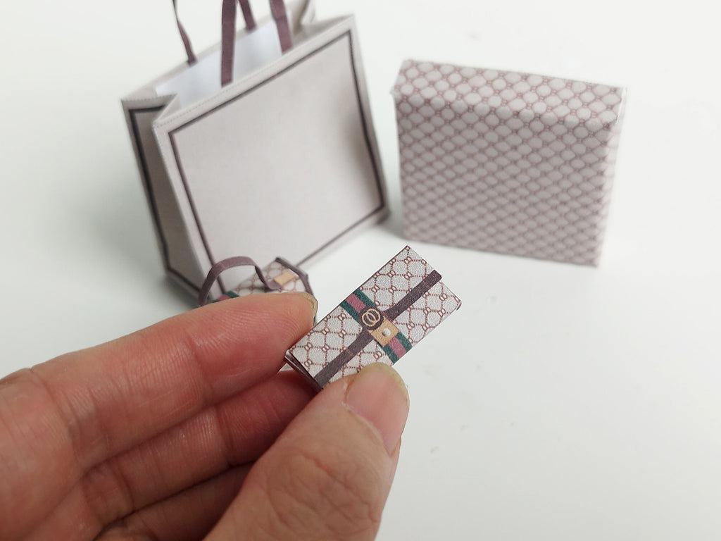A 1:6 scale printable dollhouse set featuring four luxury brand-inspired brown shopping bags, a purse, and boxes, designed for department store or luxury home decor dioramas, ideal as yearly ornaments for miniature scenes.