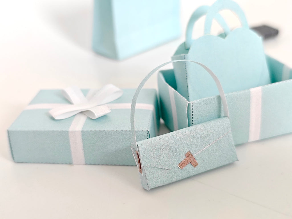 Enhance your dollhouse or department store with this 1:6 scale 5-item Sea Blue Purse and Gift Box set in black and sea blue tones. Ideal as a yearly ornament, perfect for stylish miniature displays and collectors
