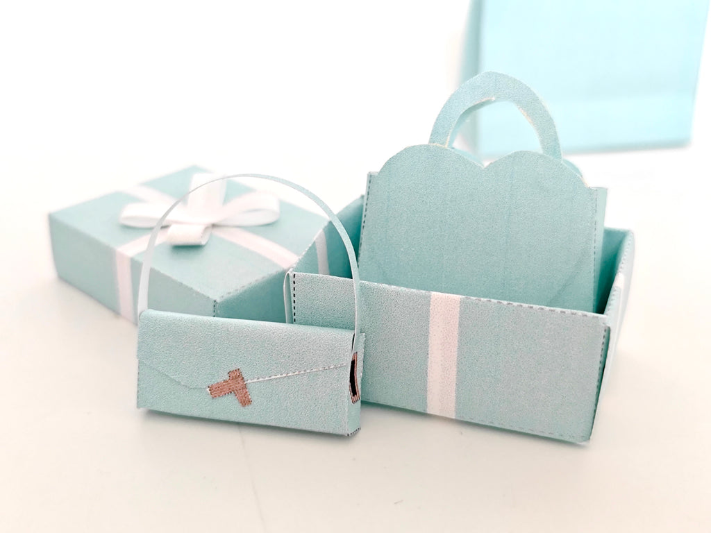 Enhance your dollhouse or department store with this 1:6 scale 5-item Sea Blue Purse and Gift Box set in black and sea blue tones. Ideal as a yearly ornament, perfect for stylish miniature displays and collectors