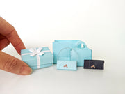 Enhance your dollhouse or department store with this 1:6 scale 5-item Sea Blue Purse and Gift Box set in black and sea blue tones. Ideal as a yearly ornament, perfect for stylish miniature displays and collectors