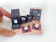 A 1:12 scale printable dollhouse Home Coffee Bar set with nine items, including a coffee machine, coffee bags, coffee cup, and desk tools, arranged for a miniature office or kitchen coffee bar diorama.