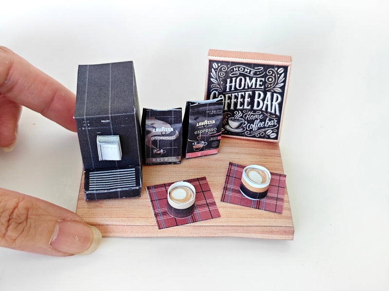 A 1:12 scale printable dollhouse Home Coffee Bar set with nine items, including a coffee machine, coffee bags, coffee cup, and desk tools, arranged for a miniature office or kitchen coffee bar diorama.