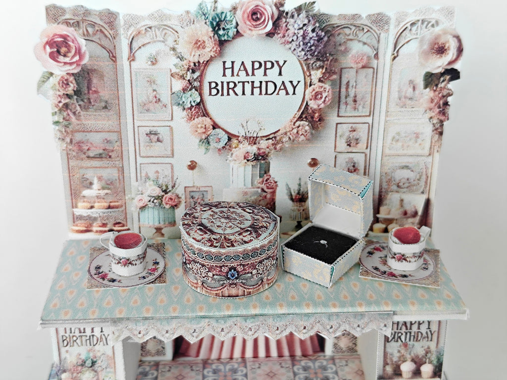 A 3D-printable STL file of a 1:12 scale vintage birthday stand DIY kit, featuring a detailed stand for displaying miniature birthday presents and cards in a dollhouse.