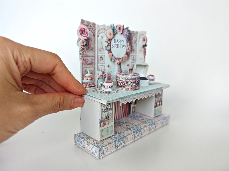 A 3D-printable STL file of a 1:12 scale vintage birthday stand DIY kit, featuring a detailed stand for displaying miniature birthday presents and cards in a dollhouse.