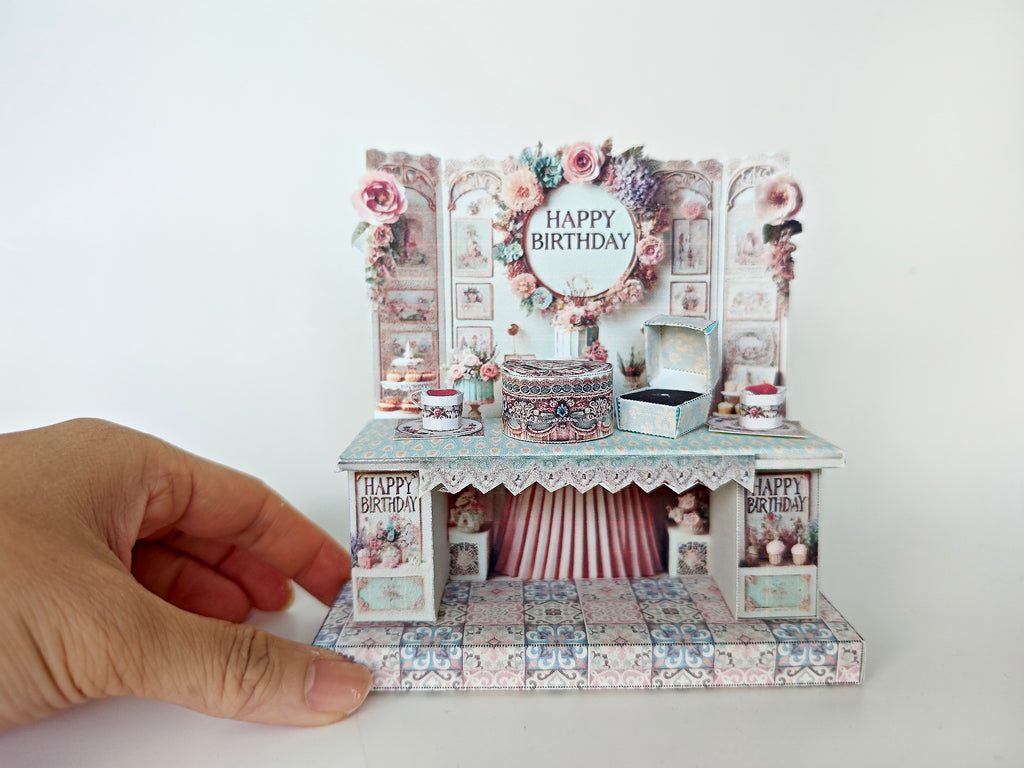A 3D-printable STL file of a 1:12 scale vintage birthday stand DIY kit, featuring a detailed stand for displaying miniature birthday presents and cards in a dollhouse.
