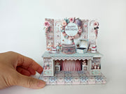 A 3D-printable STL file of a 1:12 scale vintage birthday stand DIY kit, featuring a detailed stand for displaying miniature birthday presents and cards in a dollhouse.
