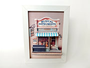 A 3D-printable STL or instant download template of a 5x7-inch pop-up frame depicting a musical instrument shop, designed with layered details for a miniature shadow box display.

