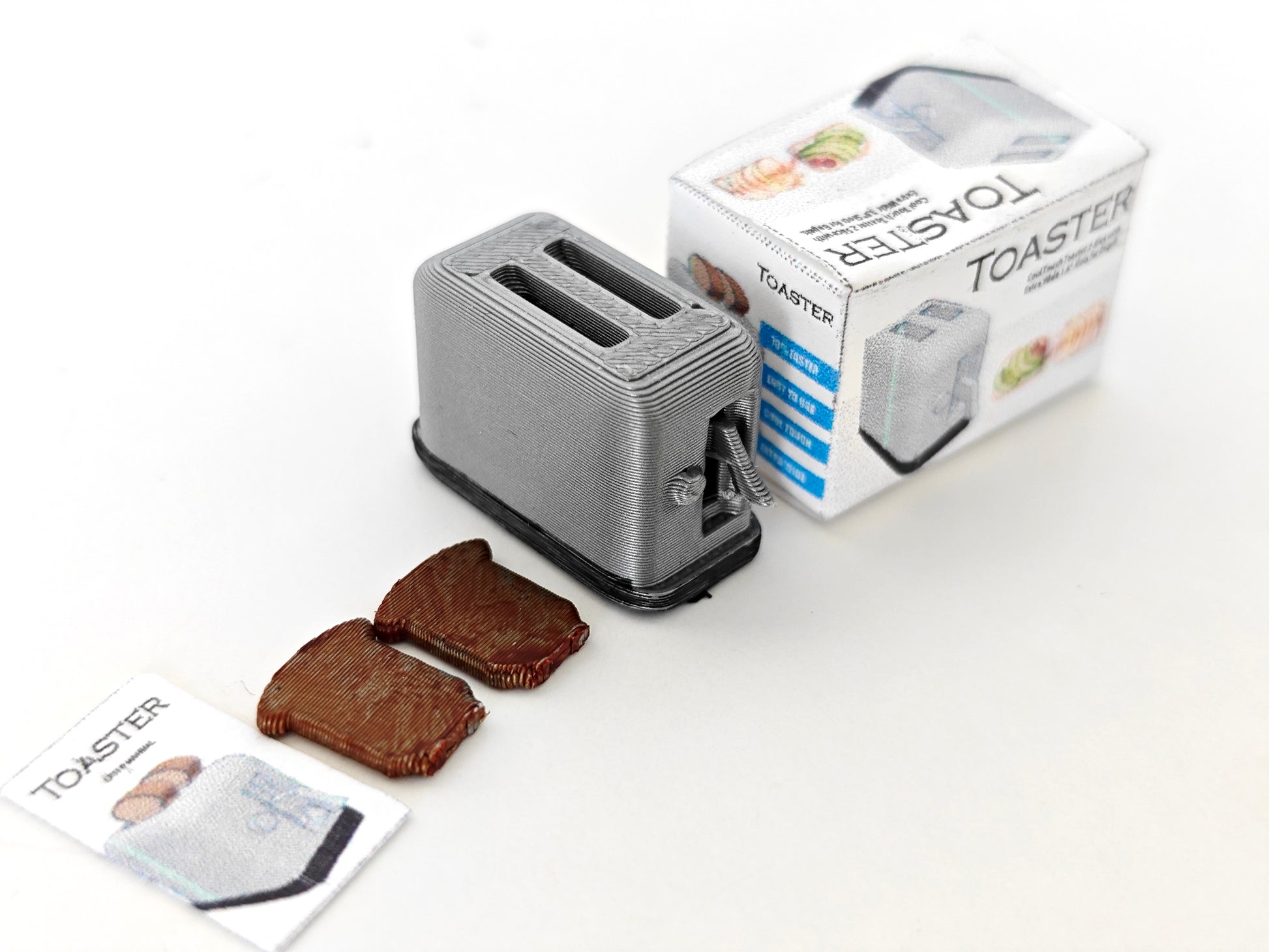 A 3D-printable STL file of a 1:12 scale miniature toaster, featuring detailed slots and buttons for a realistic dollhouse kitchen appliance