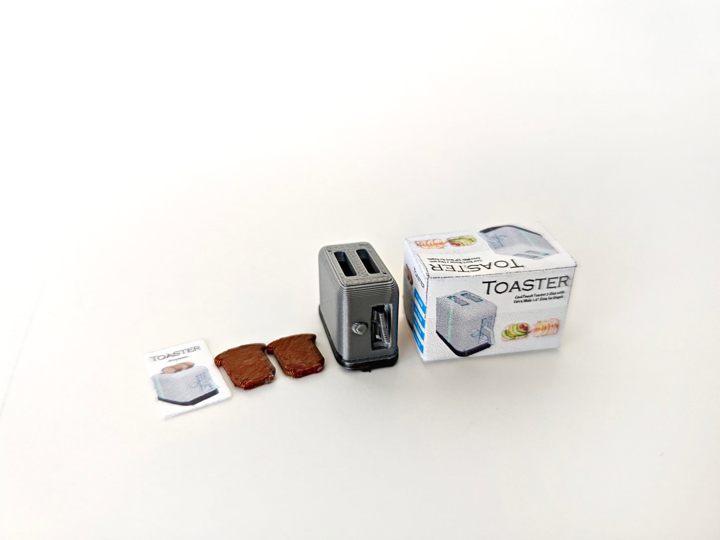 A 3D-printable STL file of a 1:12 scale miniature toaster, featuring detailed slots and buttons for a realistic dollhouse kitchen appliance