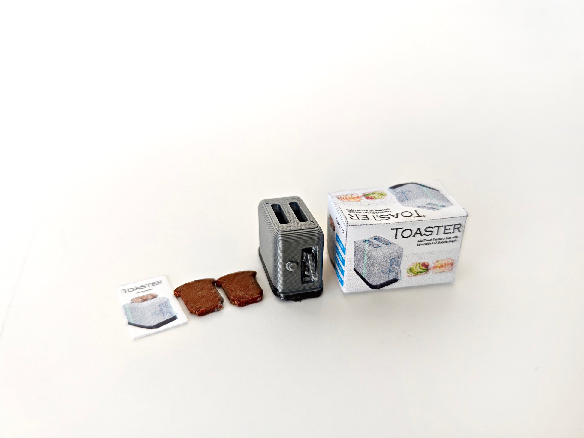A 3D-printable STL file of a 1:12 scale miniature toaster, featuring detailed slots and buttons for a realistic dollhouse kitchen appliance