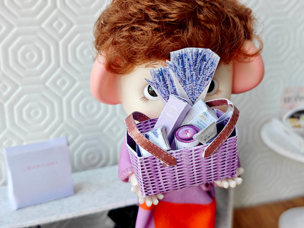Discover our 1:12 scale lavender gift basket, a charming dollhouse hamper with 11 miniature items including teas, hand cream, soaps, scented fragrance bags, and candles—perfect for a tiny spa retreat