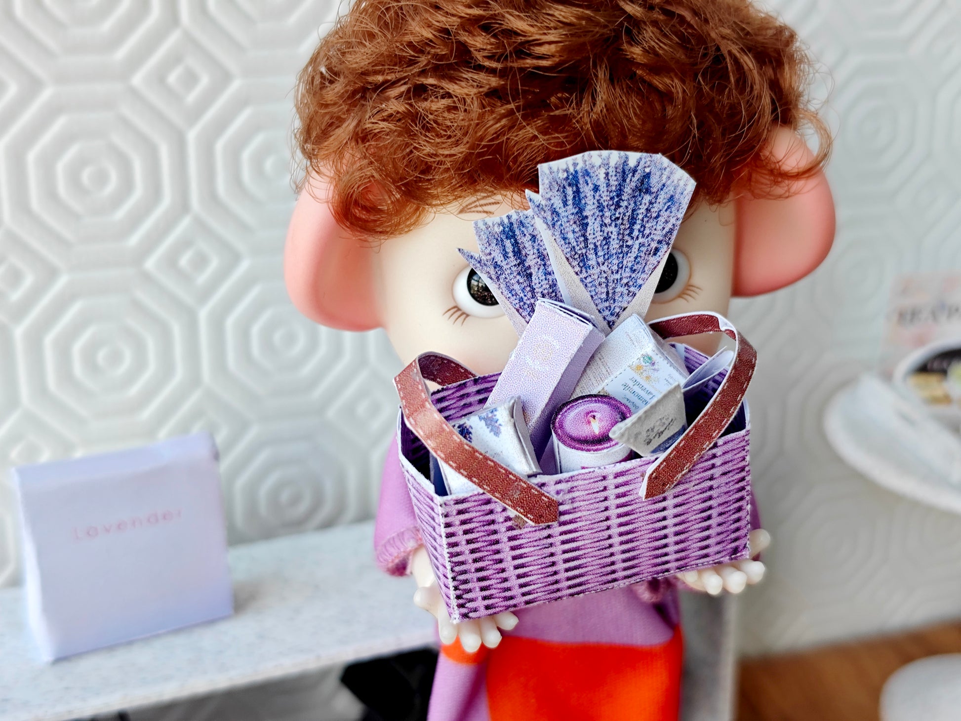 Discover our 1:12 scale lavender gift basket, a charming dollhouse hamper with 11 miniature items including teas, hand cream, soaps, scented fragrance bags, and candles—perfect for a tiny spa retreat