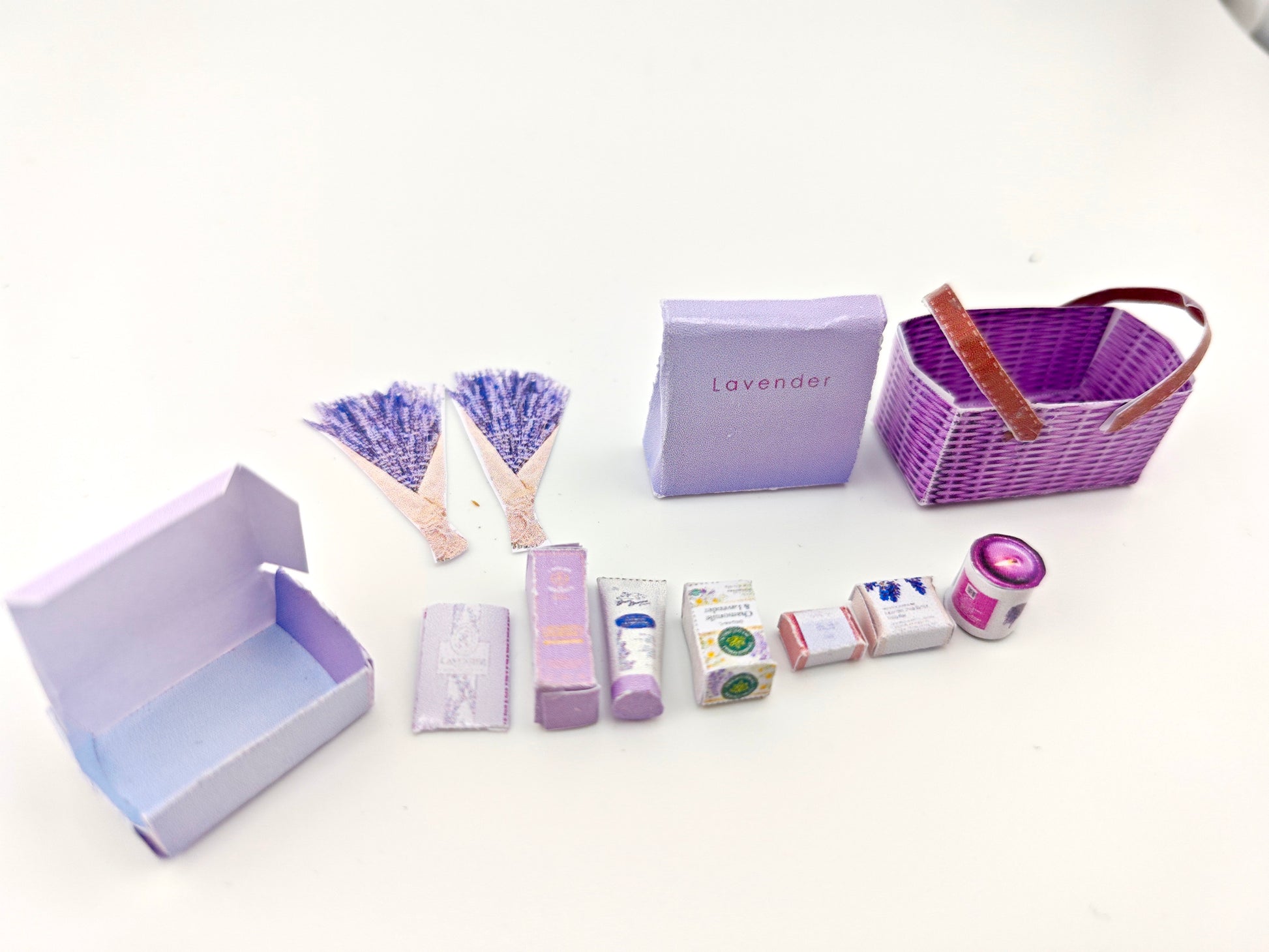 Discover our 1:12 scale lavender gift basket, a charming dollhouse hamper with 11 miniature items including teas, hand cream, soaps, scented fragrance bags, and candles—perfect for a tiny spa retreat