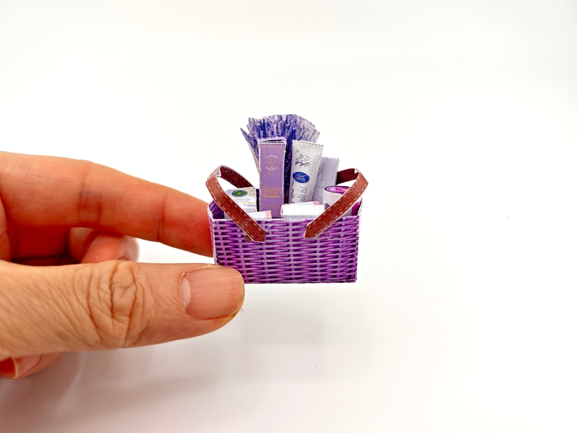 Discover our 1:12 scale lavender gift basket, a charming dollhouse hamper with 11 miniature items including teas, hand cream, soaps, scented fragrance bags, and candles—perfect for a tiny spa retreat
