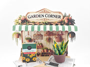 Discover the Garden Corner Miniature Stand: Create your own mini garden with plants, newspaper, potting mix, and pots. This miniature kit includes paper crafting supplies and a 7x5 frame for a charming, DIY display.