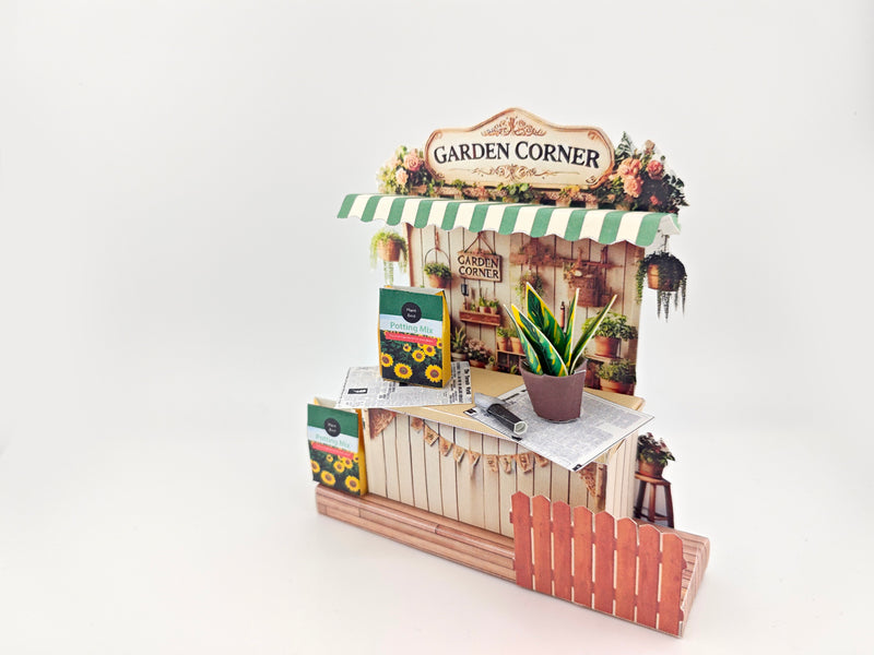Discover the Garden Corner Miniature Stand: Create your own mini garden with plants, newspaper, potting mix, and pots. This miniature kit includes paper crafting supplies and a 7x5 frame for a charming, DIY display.