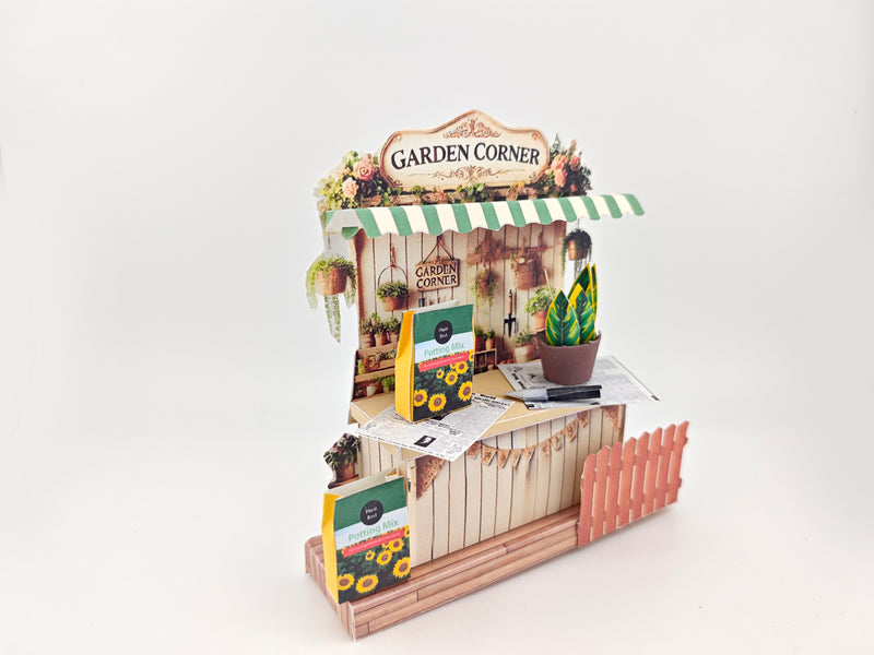 Discover the Garden Corner Miniature Stand: Create your own mini garden with plants, newspaper, potting mix, and pots. This miniature kit includes paper crafting supplies and a 7x5 frame for a charming, DIY display.