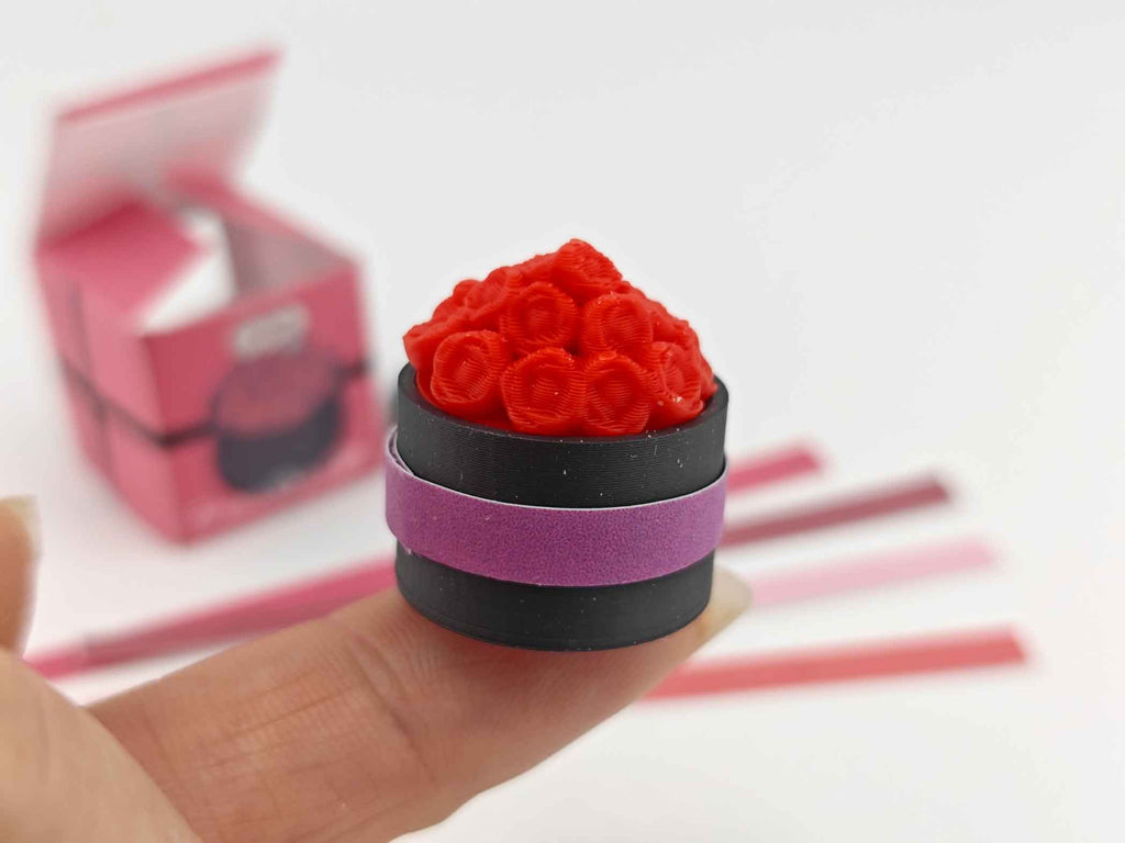 A digital rendering of a 3D printable miniature dollhouse flower box, featuring a rectangular wooden box with a grid pattern on the front. The box is accompanied by colorful strips in red, pink, and white, designed to slide into the grid for a customizable look, ideal for Mother's Day and Valentine's Day decor.