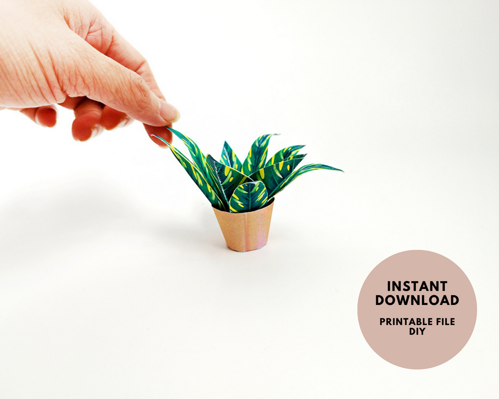 Hand holding a small papercraft plant with green and yellow leaves in a brown pot.