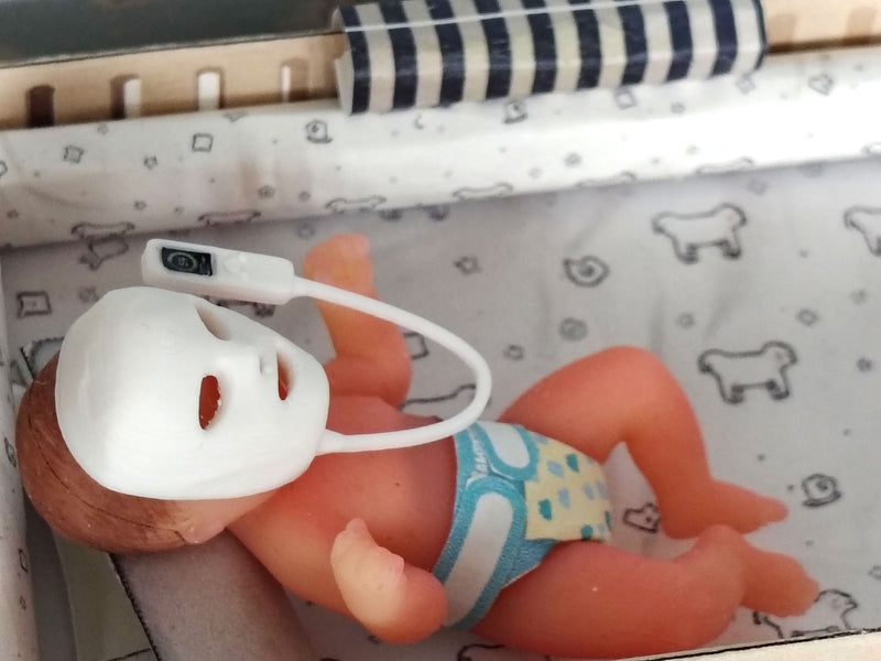 The doll has a white plastic face mask covering its eyes and nose, featuring a small black power button on the top left side of the mask frame.